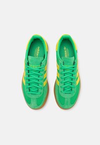 Πράσινα αθλητικά παπούτσια από διχτυωτό υλικό και σουέτ με κίτρινες ρίγες και κορδόνια, διαθέτοντας υφασμάτινη σόλα από καουτσούκ. Λογότυπο στην γλώσσα και την εσωτερική σόλα.