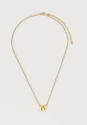 Auksinė grandinėlė su pakabuku, kuris yra „M“ raidės formos, su reguliuojamu užsegimu ant balto fono.