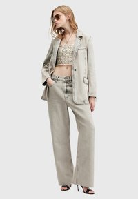 Donna che indossa un blazer in denim grigio chiaro oversize, jeans larghi abbinati, un top corto testurizzato, occhiali da sole, collana e sandali con tacco neri.