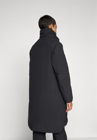 Gevoerde zwarte jas met een hoge kraag, lange silhouet en gestructureerde mouwen. Gladde textuur en minimalistisch ontwerp zonder patronen.