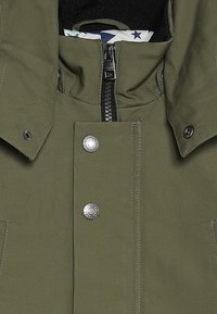 Kurtka oliwkowa z zamkiem błyskawicznym z przodu, zatrzaskami i wysokim kołnierzem. Wykonana z gładkiego materiału, z podszewką w wzory.