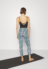 Top nero senza maniche con spalline incrociate sul retro, abbinato a leggings aderenti con un motivo floreale geometrico in verde e nero.