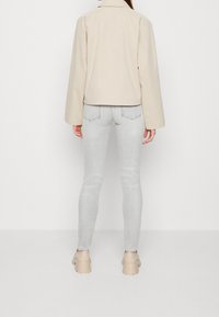 Chaqueta estructurada beige con cuello recto, combinada con jeans ajustados gris claro y zapatos de plataforma beige. Diseño minimalista con líneas limpias.