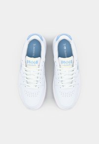 Valged nahast spordijalatsid siniste aktsentidega, millel on perforatsioonid, ümmargune ninaosa ja nöörkinnis. "LACOSTE" logo keele peal.