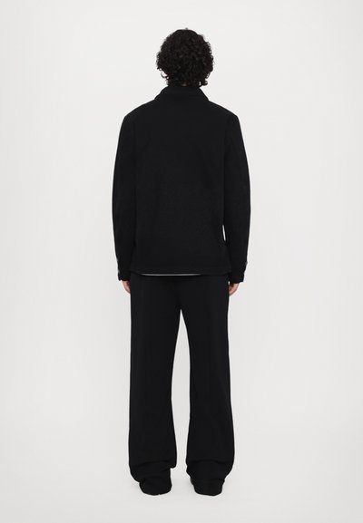 Veste noire avec une finition texturée, dotée d'un col et de détails en bouton. Associée à un pantalon noir à coupe décontractée, tous deux en tissu tissé.