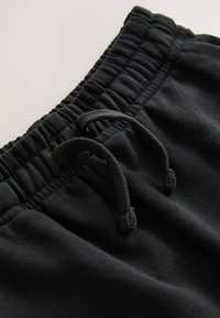 Black cotton sweatpants feature an elastic waistband with adjustable drawstrings and a smooth texture. Close-up view emphasizes details.