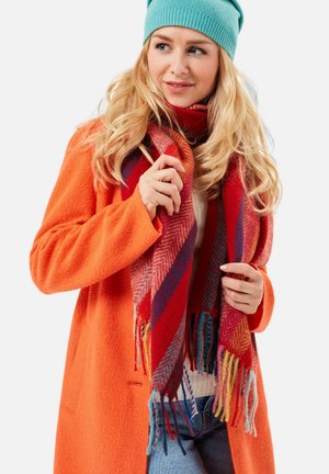 Orange wool coat, multicolored striped scarf with fringes, and a light blue knit beanie. Soft textures and bold color contrasts evident.