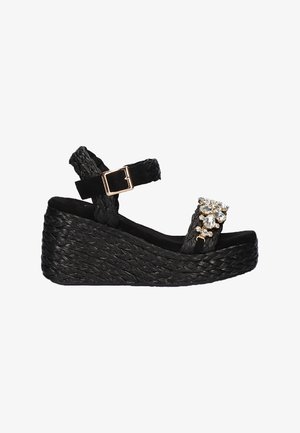Sandalia cuña negra con base de paja trenzada, tira en el tobillo y strass decorativos en la tira. Material liso y texturizado con acentos metálicos.
