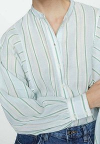 Chemise boutonnée en tissu léger et respirant ; avec des rayures verticales bleu clair et vert, un col mao et des manches avec poignets.