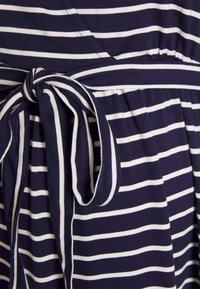 Vestido azul marinho com riscas brancas, apresentando um detalhe de cintura atada. Feito de um tecido suave, tem um corte descontraído e um design de saia fluida.