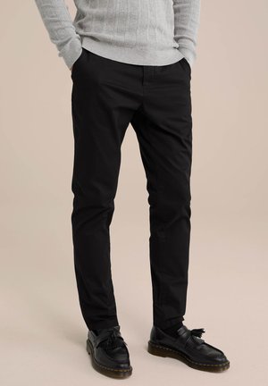 Czarne chinosy o slim fit, charakteryzujące się gładką fakturą, bocznymi kieszeniami i wywiniętymi nogawkami, zestawione z czarnymi skórzanymi butami.