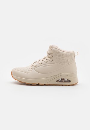 Sneaker alta beige con una toma in sintetico liscio, accenti perforati, design con lacci e ammortizzazione ad aria trasparente nella suola.