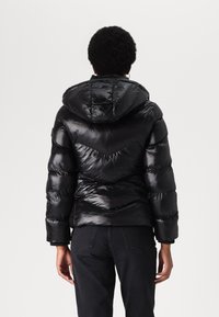 Black puffer jacket with a shiny finish, hood, and chevron quilting detail. Long sleeves and a cropped fit complete the design.