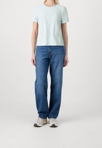 Svetle modrý top s krátkým rukávem, který má texturovaný vzor, v kombinaci s volnými modrými džíny a šedými sportovními botami. Jednoduchý kulatý výstřih.