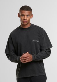 Czarna koszulka z długim rękawem o luźnym kroju. Posiada okrągły dekolt i biały nadruk "Sunday Running Club" na piersi.