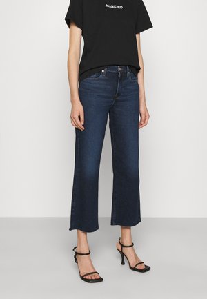 Persoon draagt donkerblauwe cropped flare jeans, zwart gestripte hoge hak sandalen en een zwart T-shirt met tekst "MANKIND".
