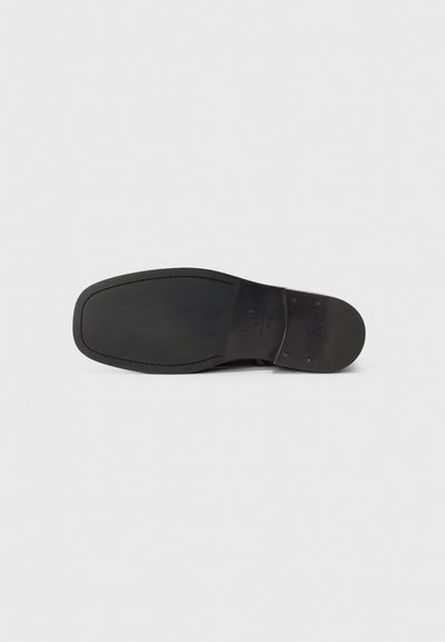 Suela de zapato de cuero negro con una textura suave, punta ligeramente redondeada y un patrón de superficie mínimo. Presenta un área de talón reforzada y costuras sutiles.