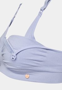 Lys lilla bh med ribbet stoff, glidelås foran, justerbare stropper og en liten metalltag. Glatt tekstur overalt.