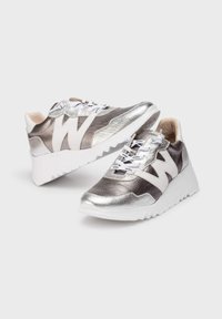 Baskets argentées métalliques et blanches avec une finition texturée, présentant un logo "W" blanc bien en vue, des lacets décoratifs et une semelle épaisse blanche.