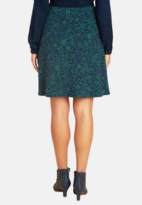 Grüner Blumenmuster-Rock aus weichem Stoff, der sich leicht von der Taille abwärts weitet. Kombiniert mit navyblauen Ankle Boots mit einem moderaten Absatz.