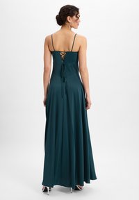 Langes Teal-Kleid aus glattem Stoff, mit einem tiefen Rückenausschnitt und Schnürdetail sowie einem fließenden Rock. Dünne Träger und ein dezenter Glanz.