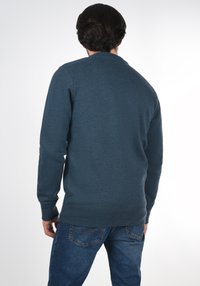 Donkerblauwe sweatshirt met een ronde hals, lange mouwen en een effen textuur. Gecombineerd met blauwe spijkerbroeken, gezien van achteren.