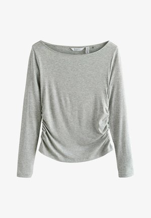Pelēka garroku blūze no mīksta materiāla, ar vaļīgu kakla izgriezumu un savākumu sānos, pievienojot tekstūru un formu.