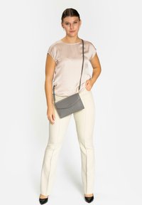 Bolso cruzado gris con una superficie texturizada, presenta un cierre con solapa y herrajes dorados, combinado con una blusa de satén clara y pantalones crema.