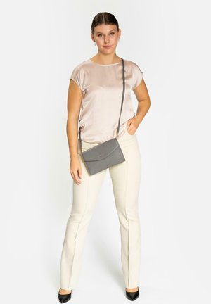 Bolso cruzado gris con una superficie texturizada, presenta un cierre con solapa y herrajes dorados, combinado con una blusa de satén clara y pantalones crema.