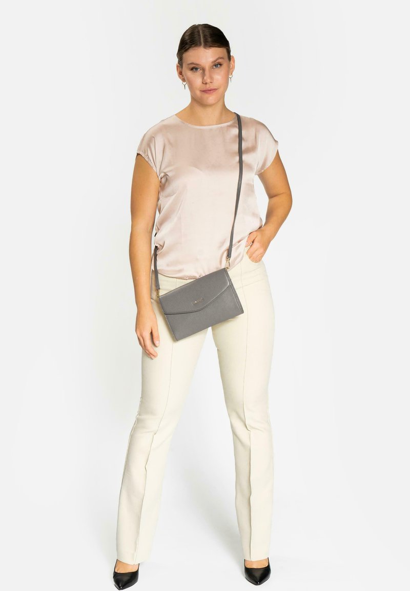 Bolso cruzado gris con una superficie texturizada, presenta un cierre con solapa y herrajes dorados, combinado con una blusa de satén clara y pantalones crema.