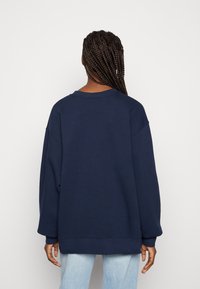 Granatowy, oversize'owy sweter z okrągłym dekoltem, opuszczonymi ramionami i ściągaczami na rękawach. Miękki materiał, prosty design, bez widocznych wzorów.