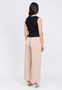 Top nero senza maniche a costine abbinato a pantaloni beige a gamba larga in tessuto testurizzato con fascia elasticizzata in vita, indossato con sandali con tacco bianchi.