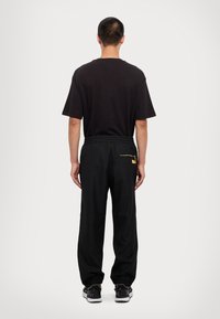 Black t-shirt with short sleeves paired with black jogger pants featuring elastic cuffs and a gold zippered back pocket.