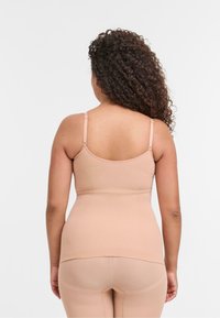 Top sin mangas nude con tirantes ajustables, textura suave, diseño ajustado y escote redondo en la parte posterior. Combinado con leggings ajustados a juego.