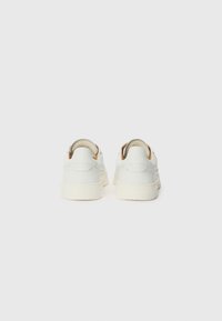 Zapatillas de deporte de cuero blanco con un acabado texturizado, que presentan una suela de goma color crema y un acento marrón en el talón.