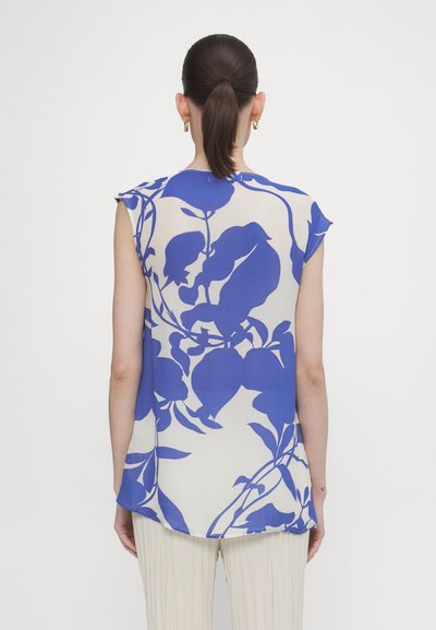 Mouwloos topje van doorzichtig stof met een blauw bloemenpatroon op een crèmekleurige achtergrond; gebogen zoom en een ontspannen pasvorm.