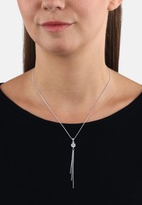 Silverhalsband med en rund hänge och kaskadkedjor, bärs på en svart skjorta som framhäver detaljerna på pendeln.