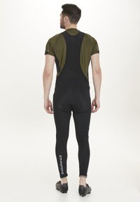 Svarta cykelbyxor med vadderad sits och en grön kortärmad tröja, med en åtsittande design och logodetalj på vänster ben.