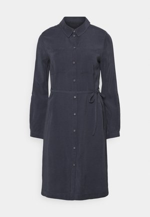 Robe boutonnée à manches longues bleu foncé avec col, deux poches poitrine et une fine ceinture à la taille sur un fond blanc.