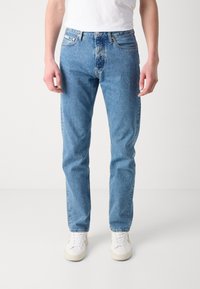 Jeansi din denim de un albastru deschis, cu croială dreaptă, design standard cu cinci buzunare și decolorare subtilă pe față. Asortați cu adidași albi.