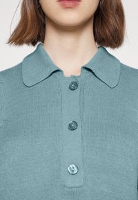 Pletené polo tričko v jemné tyrkysové barvě, s límečkem a třemi zakulacenými knoflíky. Texturovaná látka s jemným žebrovaným vzorem.