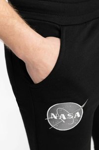 Schwarze Sweatpants mit einer Fronttasche, featuring einem grauen NASA-Logo, das auf dem linken Oberschenkel gestickt ist. Weiches Baumwollmaterial mit einer lockeren Passform.