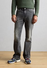 Dunkelgraue Jeans mit verwaschenem Finish, geradem Schnitt, Fünf-Taschen-Design, Metallknopfverschluss, kombiniert mit mehrfarbigen Sportschuhen.