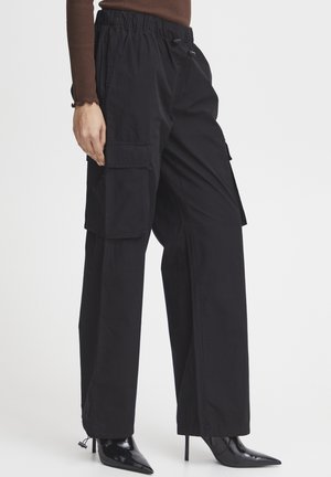 Pantaloni cargo negri, cu talie elastică și șnur de ajustare, având buzunare laterale și tăietură conică. Purtați cu pantofi cu toc înalt negri.