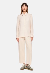 Light pink long-sleeve button-up shirt with a collar, paired with loose beige trousers and patterned black and white sneakers.
