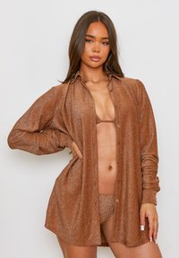 Camisa de manga larga de bronce metalizado con cierre de botón, usada sobre un conjunto de bikini a juego; textura suave con un ajuste ligeramente holgado.