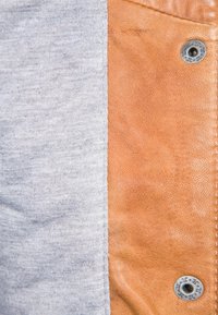 Twee stoffen: grijze katoen aan de linkerkant, beige leer aan de rechterkant. Voorzien van een zilveren drukknop op hetleren gedeelte. Soepele textuur, contrasterende kleuren.