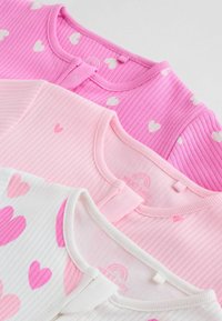 Trzy dziecięce bluzeczki w odcieniach różu: jedna z białymi wzorami serc, druga jednolita różowa i biała z różowymi serduszkami. Prążkowana faktura i okrągłe kołnierzyki.