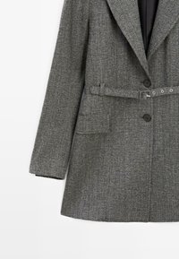 Grau melierter Wollmischmantel mit maßgeschneidertem Design, scharfen Revers, Knöpfen, einem taillierten Bund und einer einzelnen Brusttasche; strukturierte Stoffoberfläche.