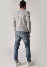 Světle šedá dlouhá košile v kombinaci se středně modrými džíny, nabízející klasický střih a vyhrnuté manžety. Bílé tenisky dotvářejí vzhled.